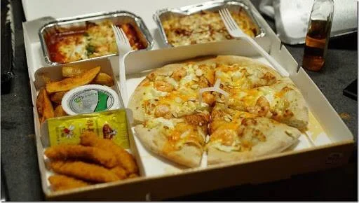 Caja con pizza de queso cortada en porciones, papas fritas, bocadillos empanados y dos bandejas de pasta al horno.