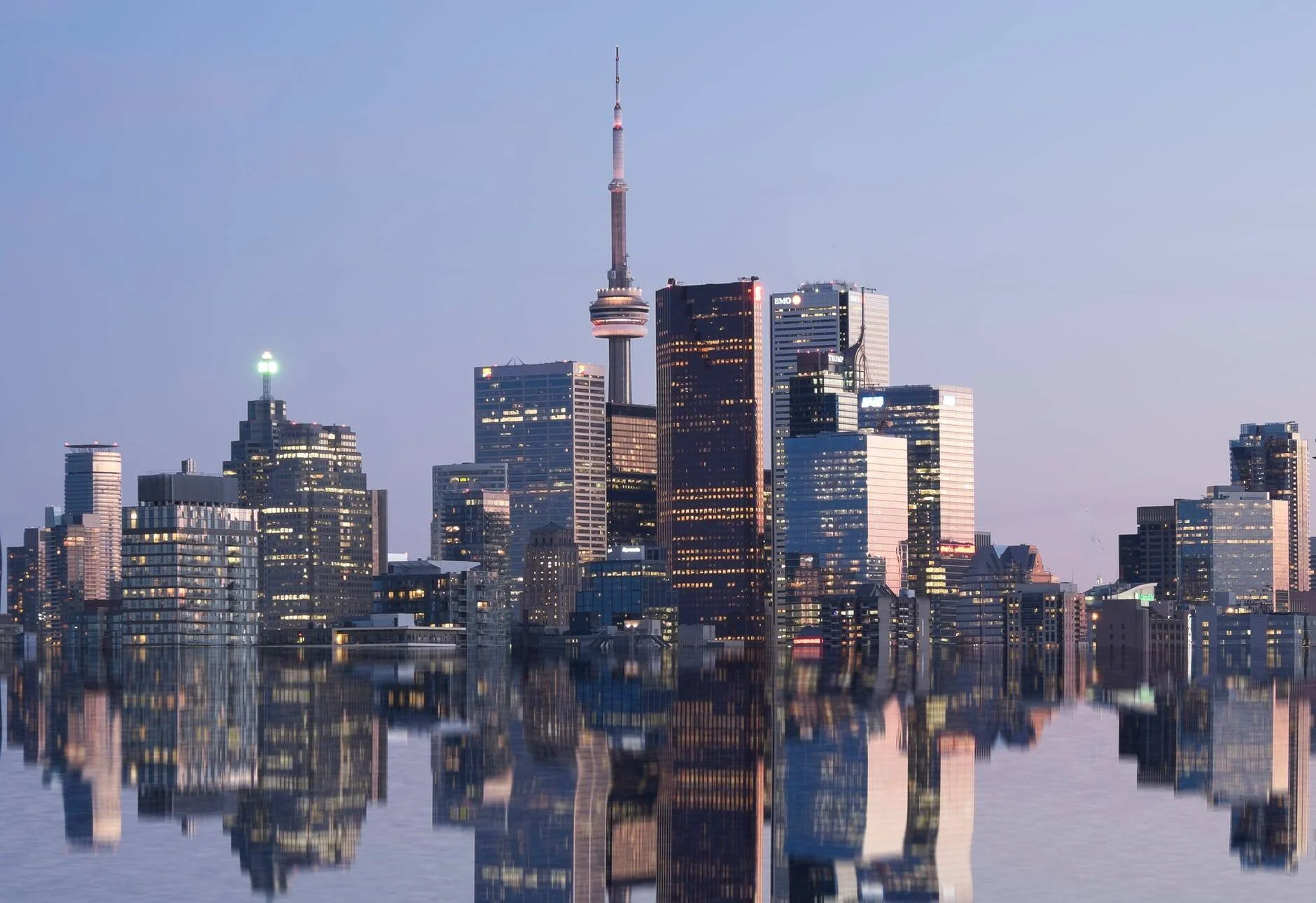 Horizonte urbano de Toronto con la CN Tower y rascacielos iluminados reflejados en el lago al anochecer.