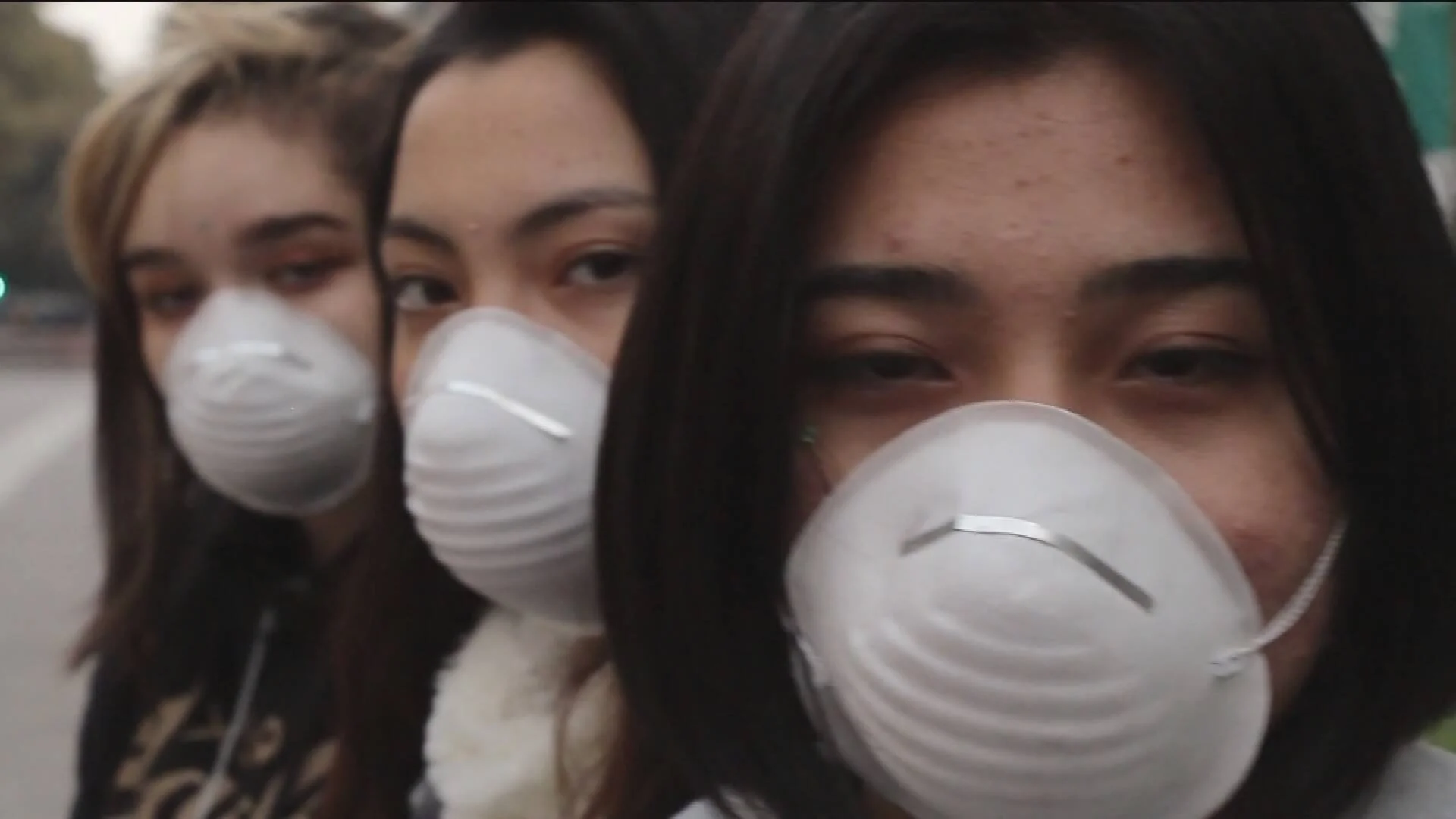Tres jóvenes con mascarillas de protección respiratoria blancas tipo N95 en la calle.