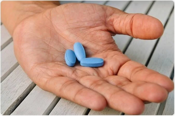 Una mano sostiene tres pastillas de color azul sobre una superficie de madera.