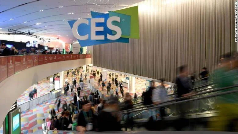 Asistentes recorren el salón principal de la feria tecnológica CES bajo un gran cartel con el logo del evento.