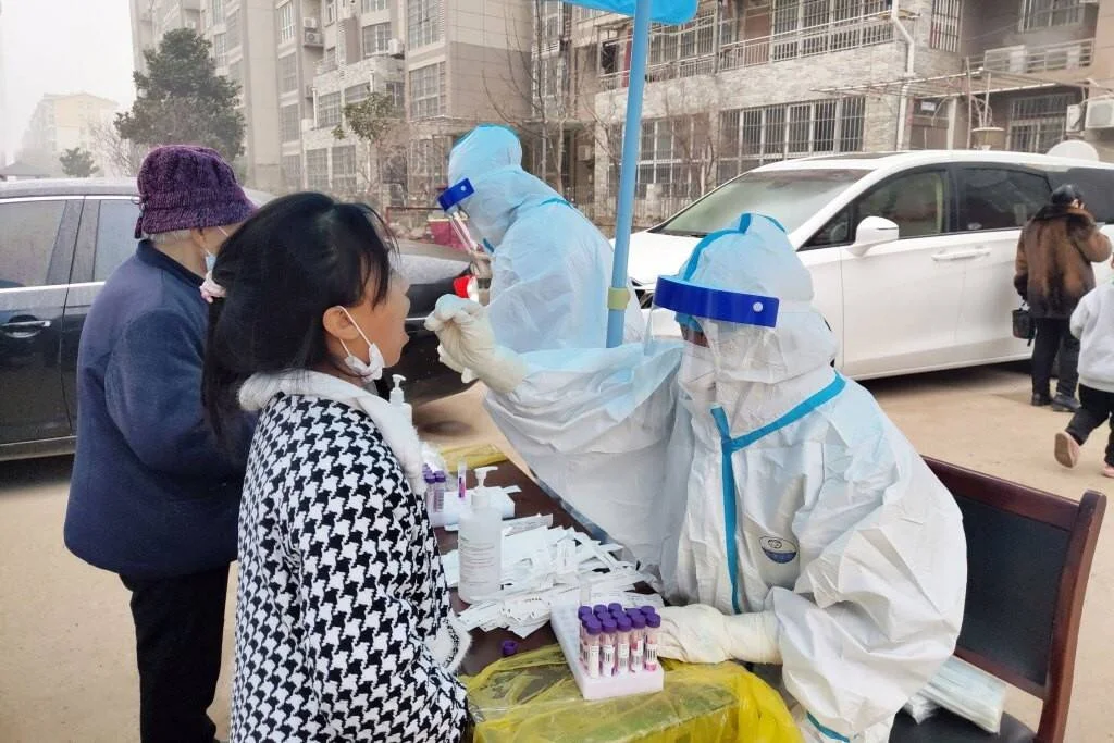 Trabajadores de salud con trajes de protección toman muestras de hisopado a ciudadanos en un puesto de pruebas al aire libre.