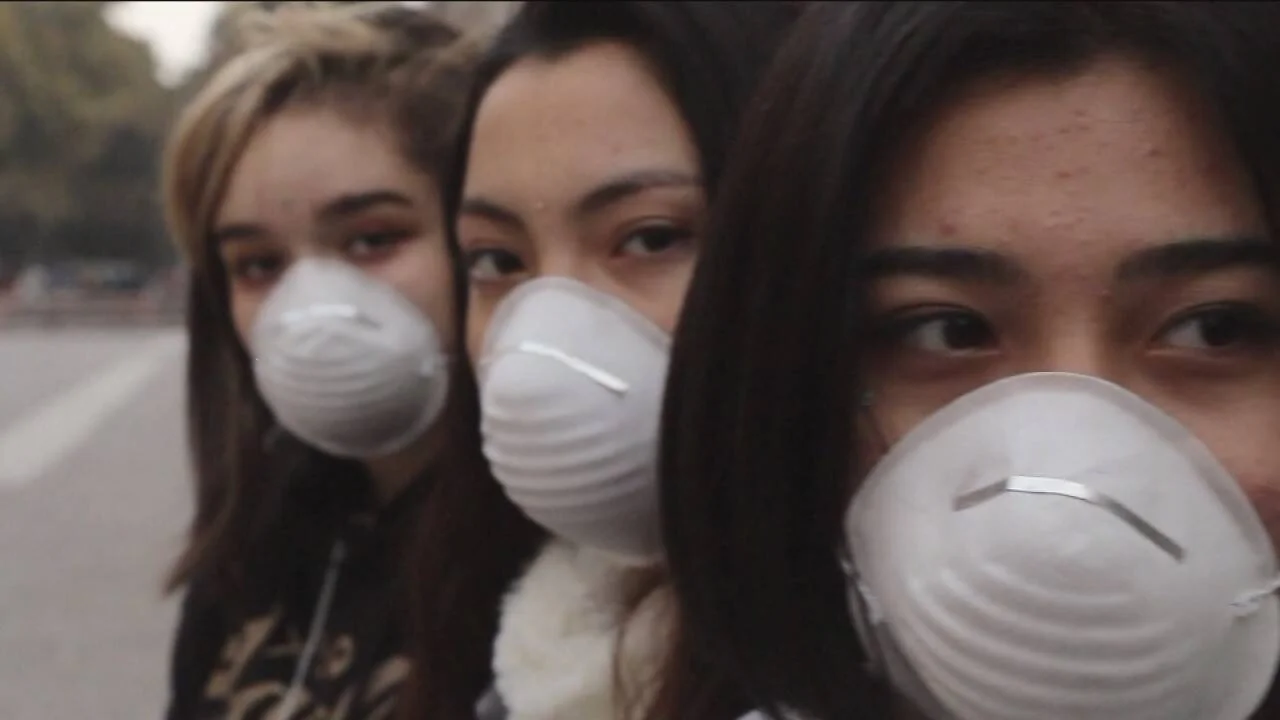 Tres jóvenes usan mascarillas de protección respiratoria en un entorno urbano al aire libre.