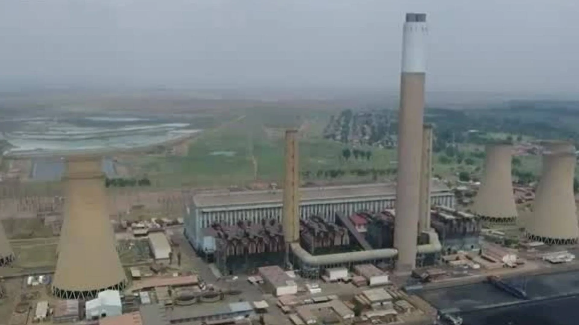 Vista aérea de una gran central térmica con torres de refrigeración y altas chimeneas en un entorno industrial.