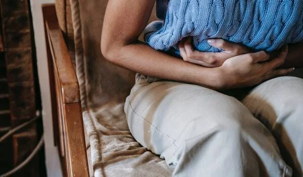 Persona sentada sosteniéndose el abdomen con ambas manos, en señal de dolor o malestar estomacal.