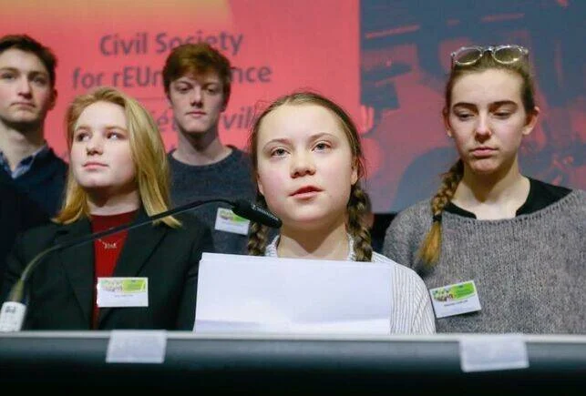 Una joven habla en un micrófono ante una conferencia de sociedad civil, acompañada por otros jóvenes activistas.