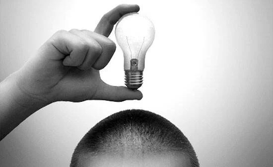 Una mano sostiene una bombilla incandescente sobre la cabeza de una persona, simbolizando una idea o pensamiento creativo.