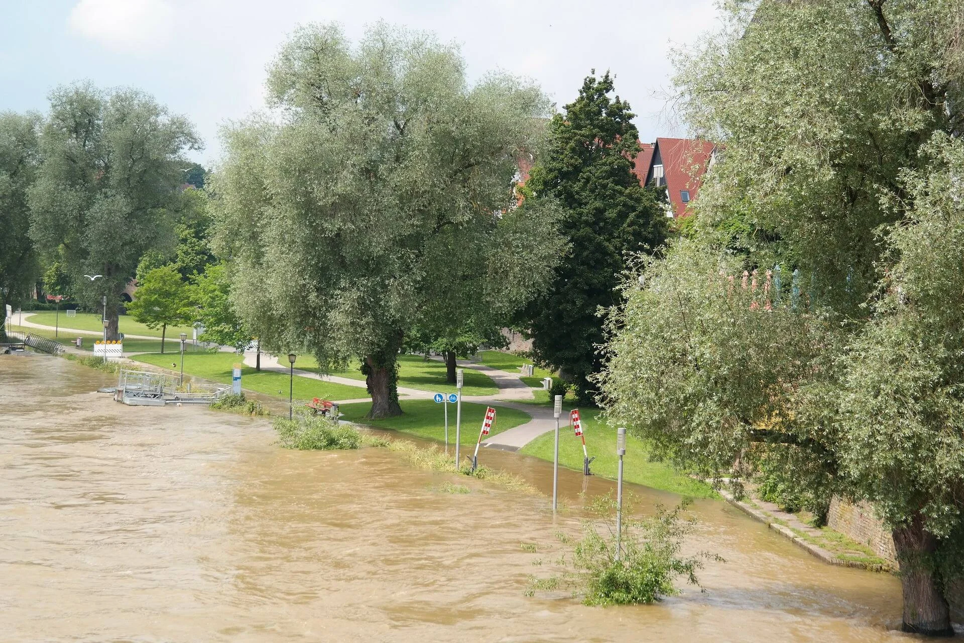 Un río con agua turbia y crecida desborda su cauce e inunda el paseo peatonal y zonas verdes de una localidad.