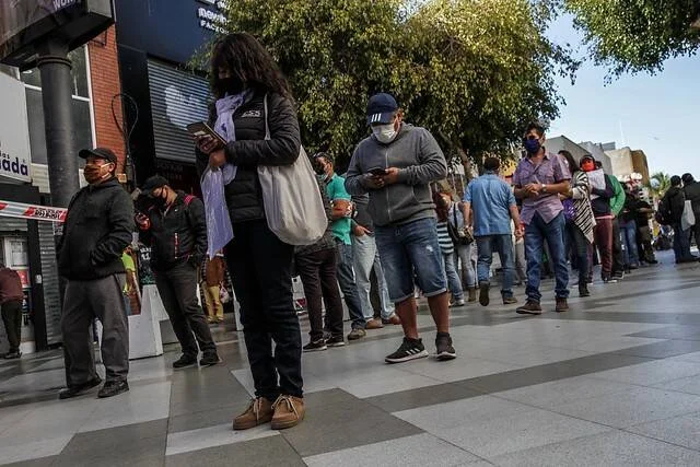 Larga fila de personas con mascarillas esperando en una acera de la ciudad durante la pandemia de COVID-19.