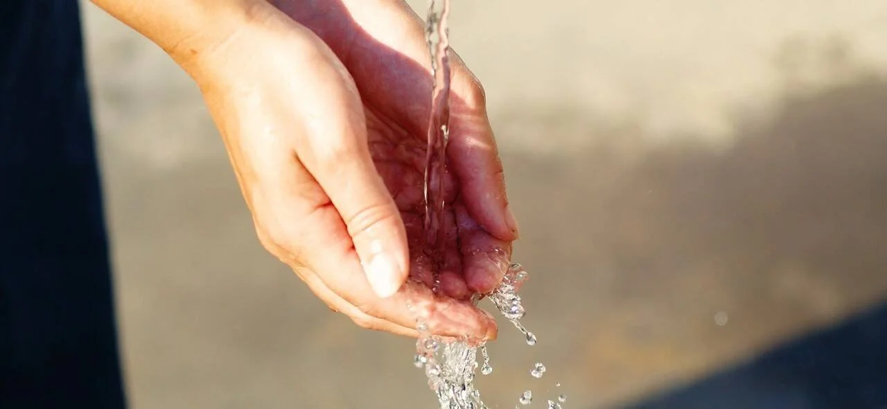 Dos manos ahuecadas reciben un chorro de agua limpia que se derrama entre los dedos al aire libre.