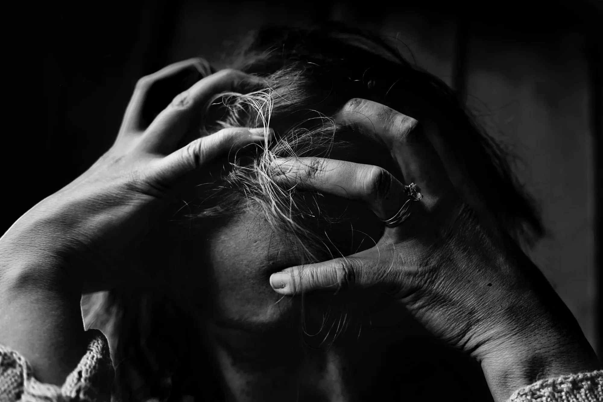 Mujer sujeta su cabeza con ambas manos en un gesto de angustia o desesperación, en blanco y negro.
