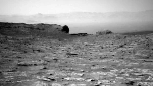 Fotografía en blanco y negro de la superficie de Marte con terreno rocoso, colinas y montañas difuminadas en el horizonte.