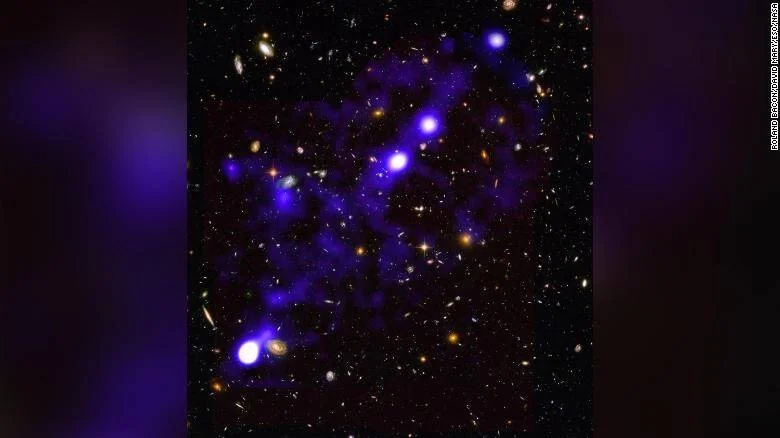 Filamentos de gas intergaláctico de color azul-violeta conectan grupos de galaxias brillantes sobre un fondo de espacio profundo.