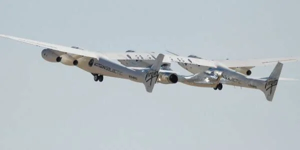 Aeronave nodriza de Virgin Galactic con doble fuselaje despega llevando una nave espacial acoplada bajo sus alas.