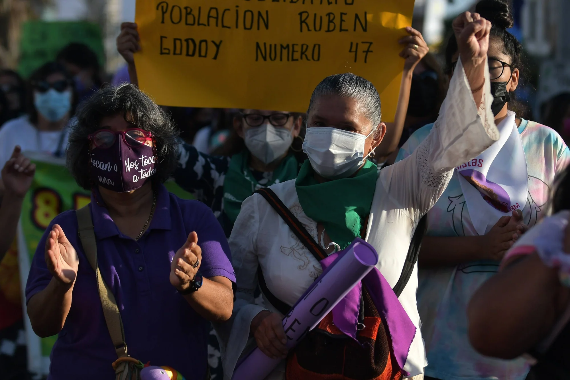 Mujeres con cubrebocas y pañuelos verdes participan en una marcha feminista con carteles y puños en alto.