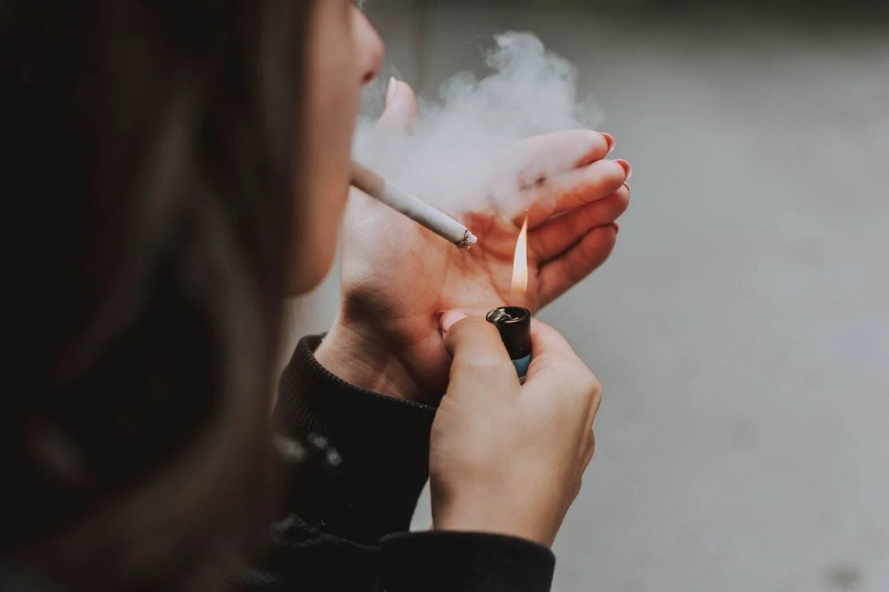 Una persona enciende un cigarrillo con un encendedor mientras exhala humo.