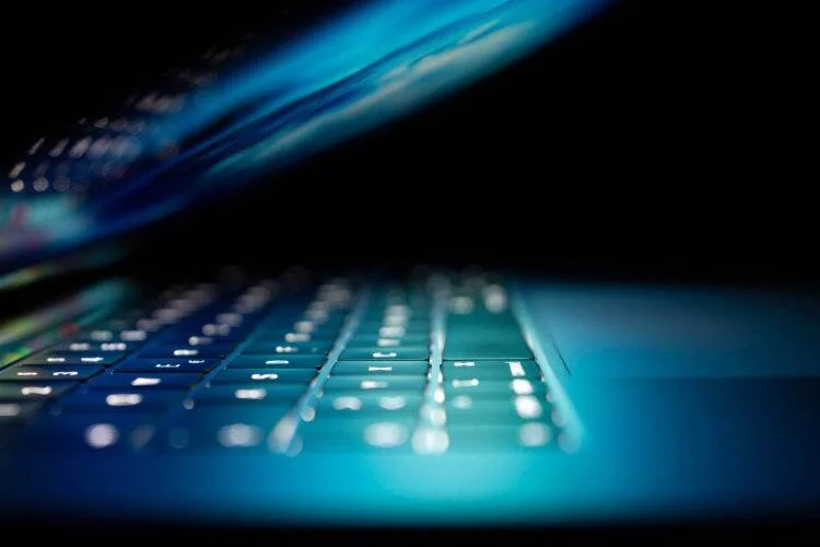 Teclado retroiluminado de una laptop emitiendo luz azul turquesa en un entorno oscuro.