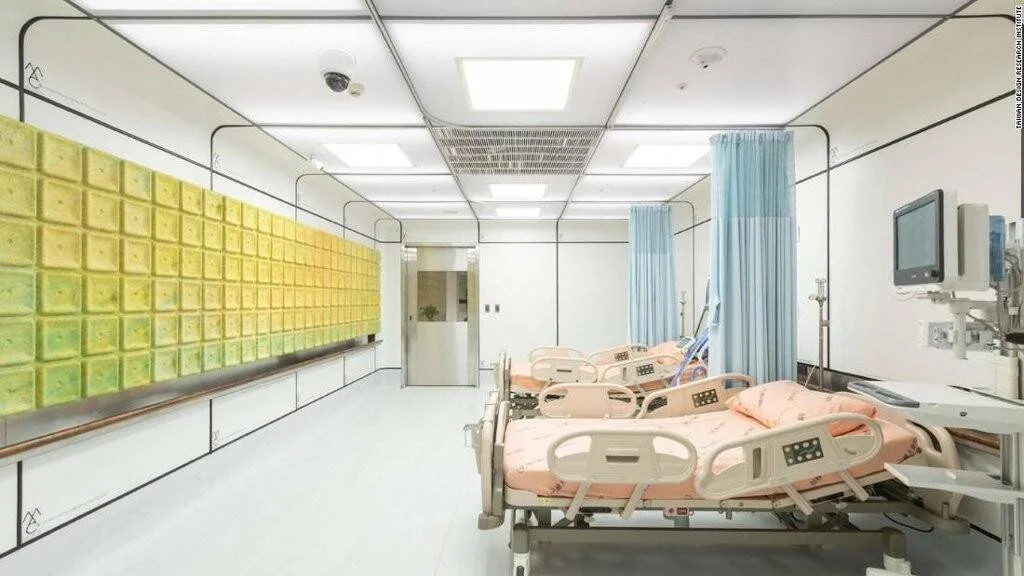 Sala de hospital con varias camas clínicas de color salmón, cortinas azules divisorias y una llamativa pared de paneles amarillo-verdes.