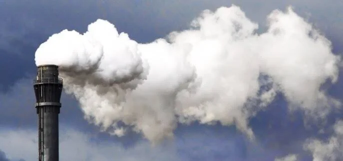Chimenea industrial expulsando una gran columna de humo blanco contra un cielo nublado.