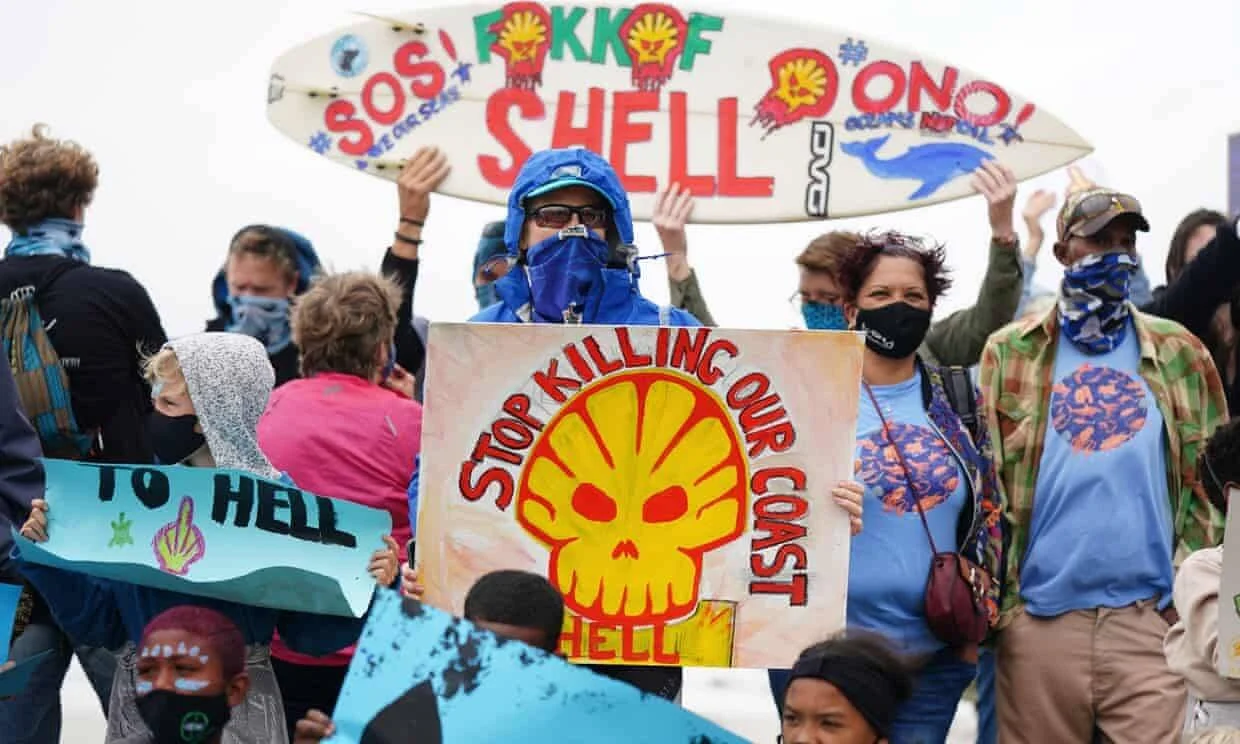 Manifestantes sostienen carteles y una tabla de surf con consignas contra Shell pidiendo detener la explotación petrolera en la costa.