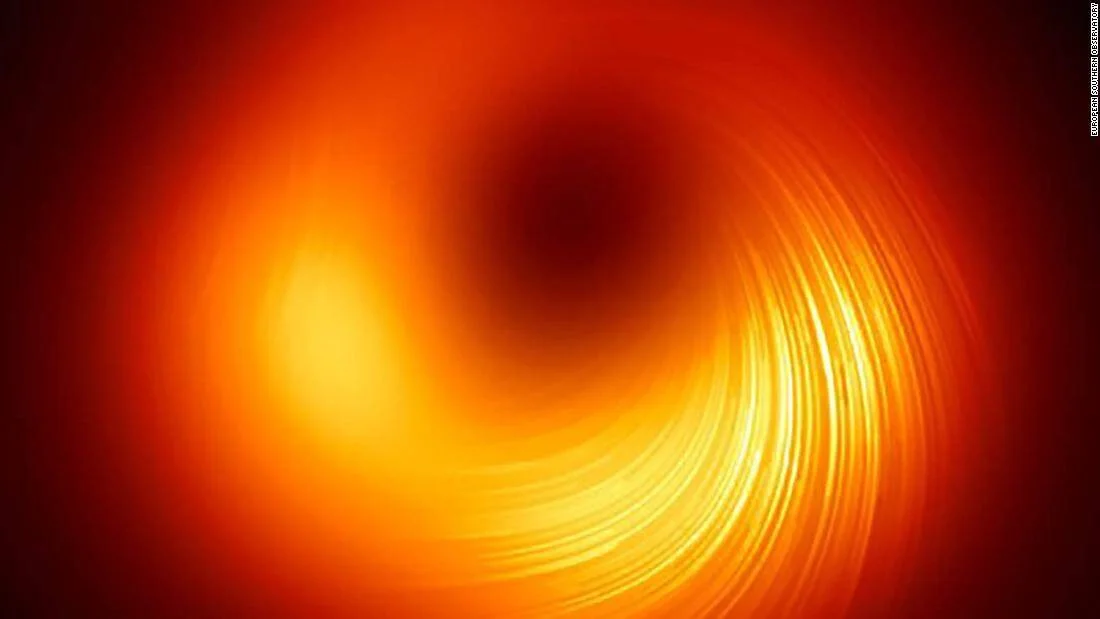 Imagen de un agujero negro rodeado por un anillo de plasma naranja y dorado con líneas de campo magnético visibles, captada por el Observatorio Europeo Austral.