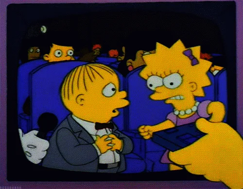 Lisa Simpson reacciona molesta ante Ralph Wiggum sentados en un cine, en una escena animada de Los Simpson.
