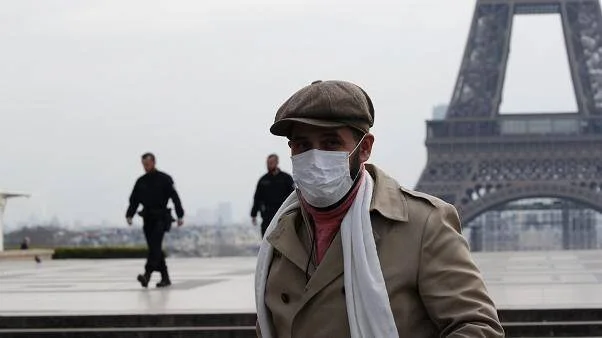 Hombre con mascarilla quirúrgica y bufanda blanca camina frente a la Torre Eiffel en París durante la pandemia.