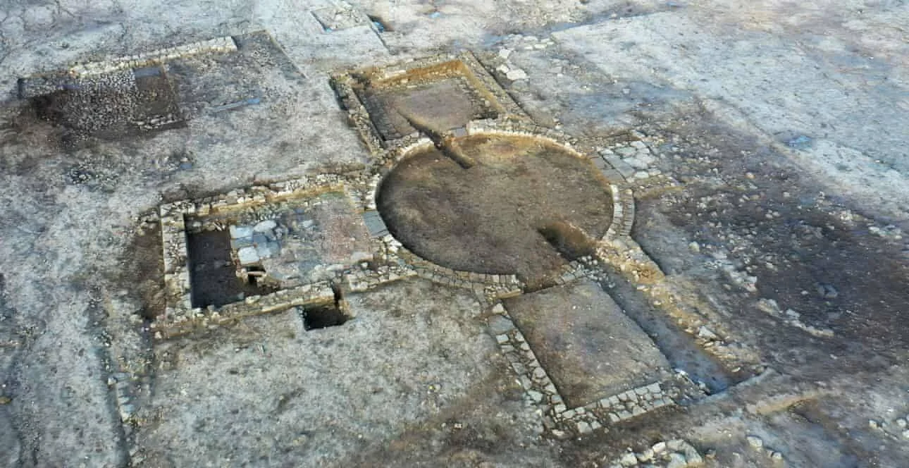 Vista aérea de un yacimiento arqueológico con muros de piedra que delimitan una gran estructura circular central y habitaciones rectangulares adyacentes.