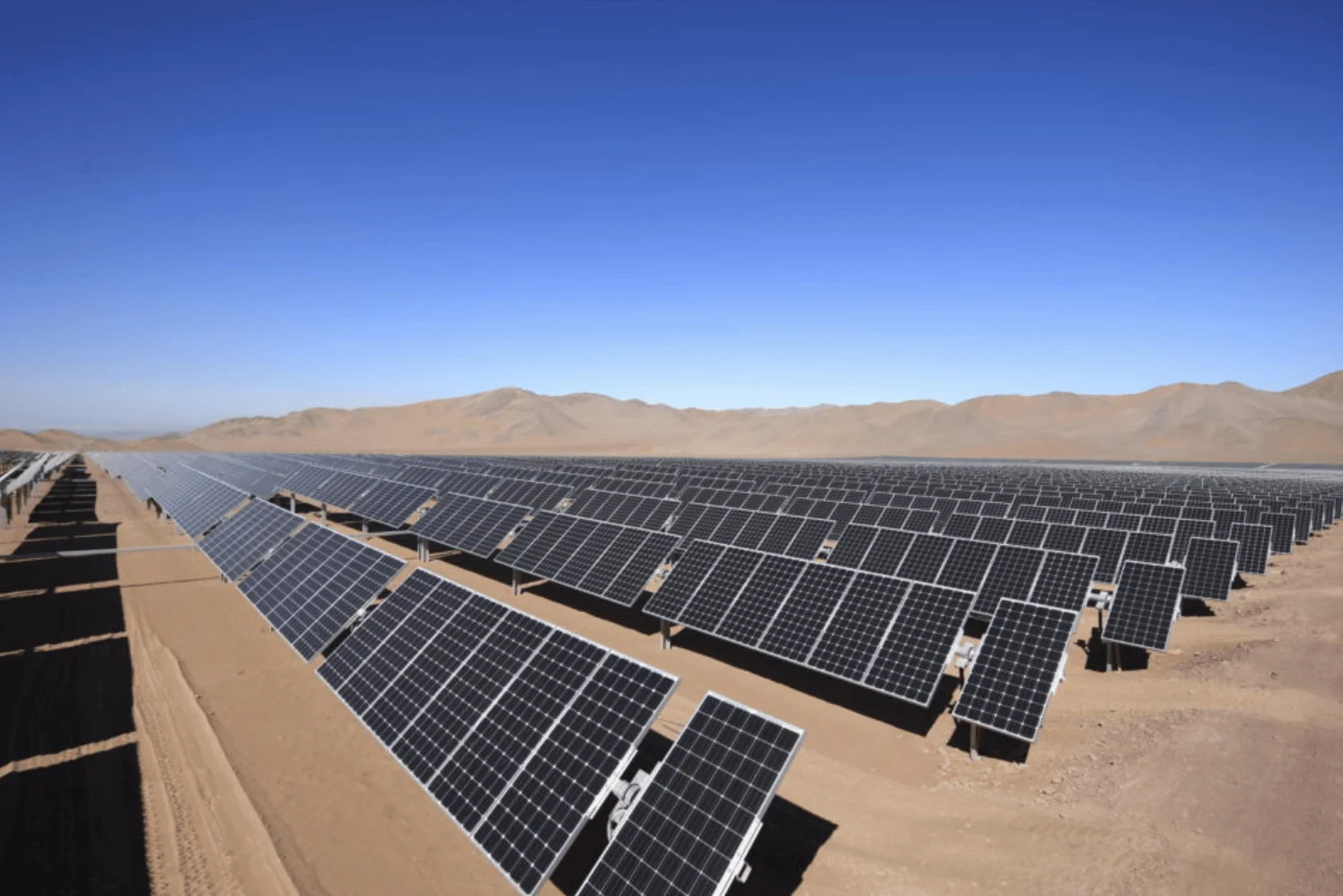Extenso campo de paneles solares fotovoltaicos instalados en un desierto árido con montañas al fondo y cielo despejado.