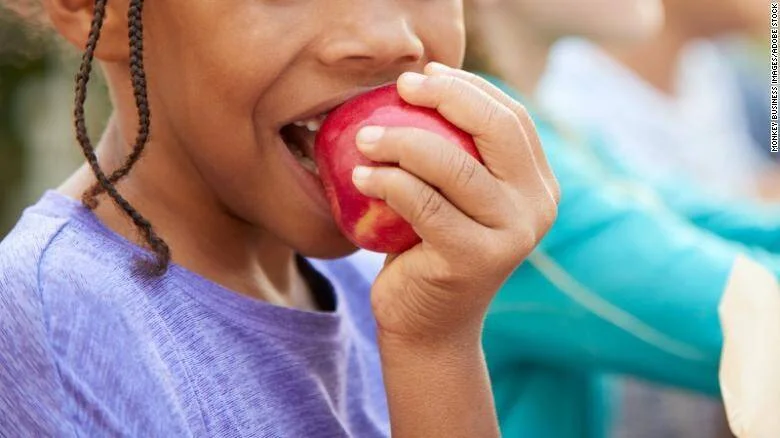 Una niña muerde una manzana roja fresca, mostrando hábitos de alimentación saludable en la infancia.