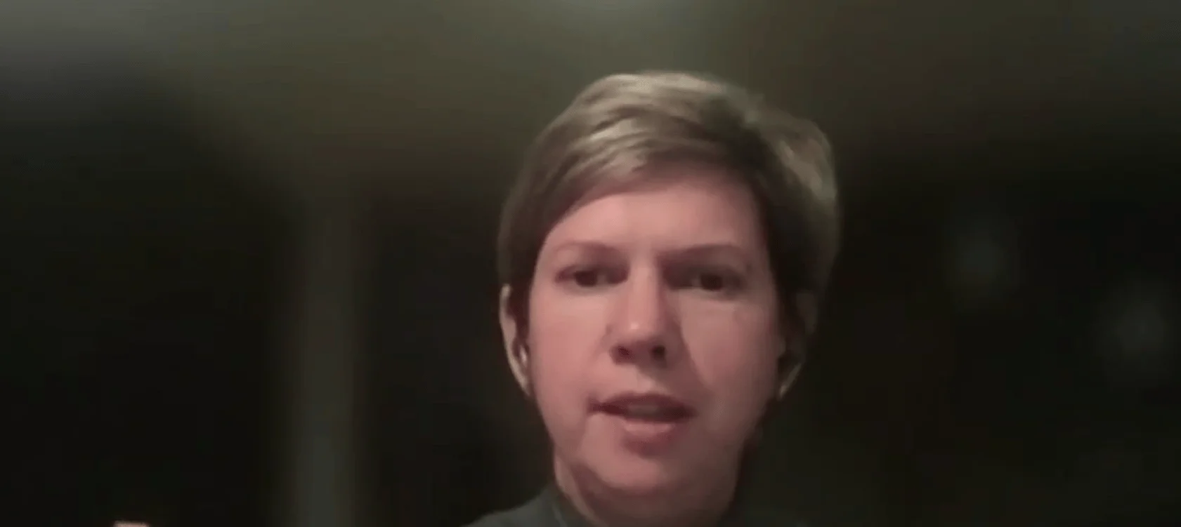 Persona de cabello corto castaño hablando frente a una cámara en un entorno oscuro.