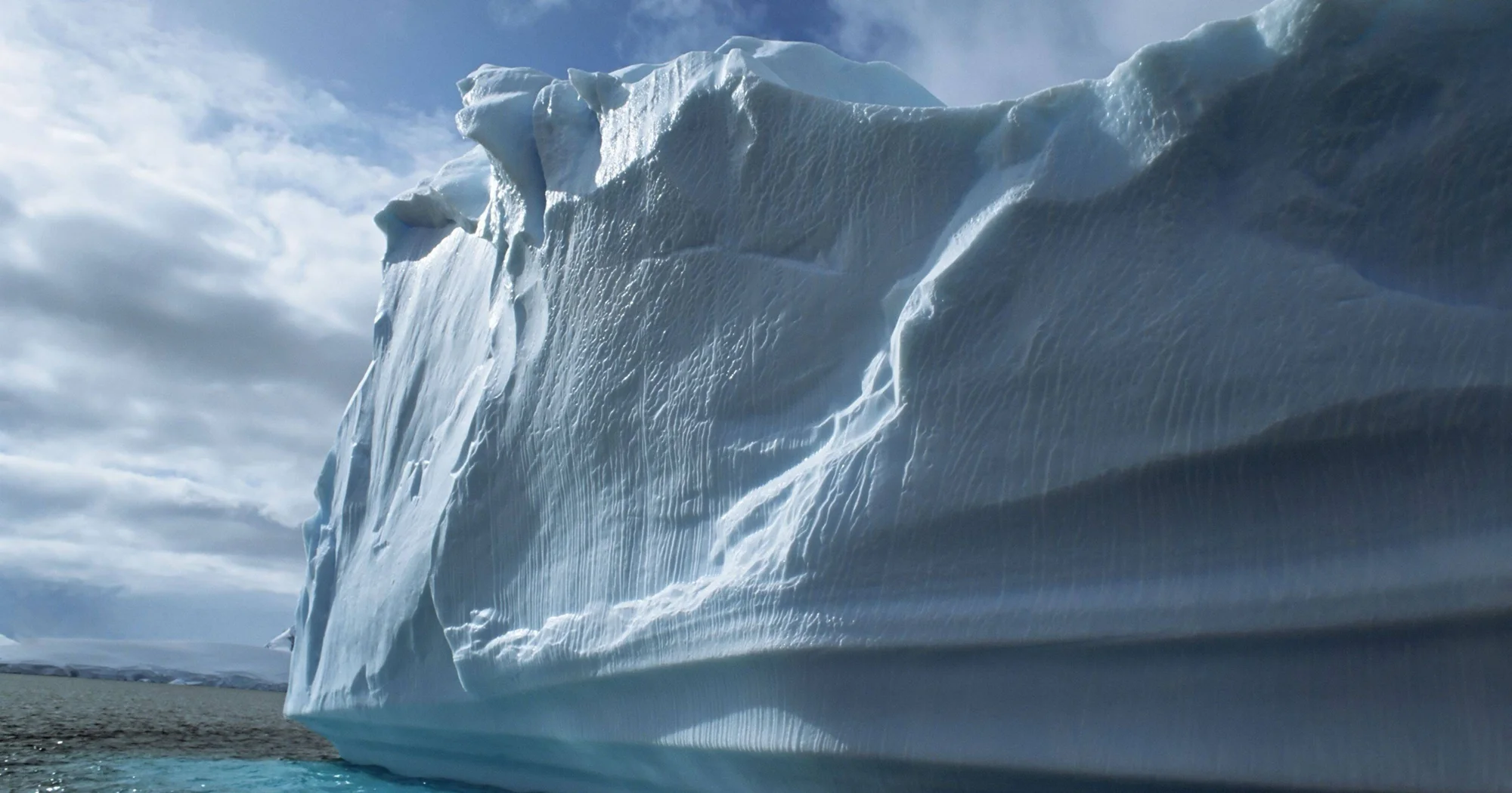 Vista cercana de un gran iceberg con superficie erosionada flotando en aguas frías bajo un cielo nublado.