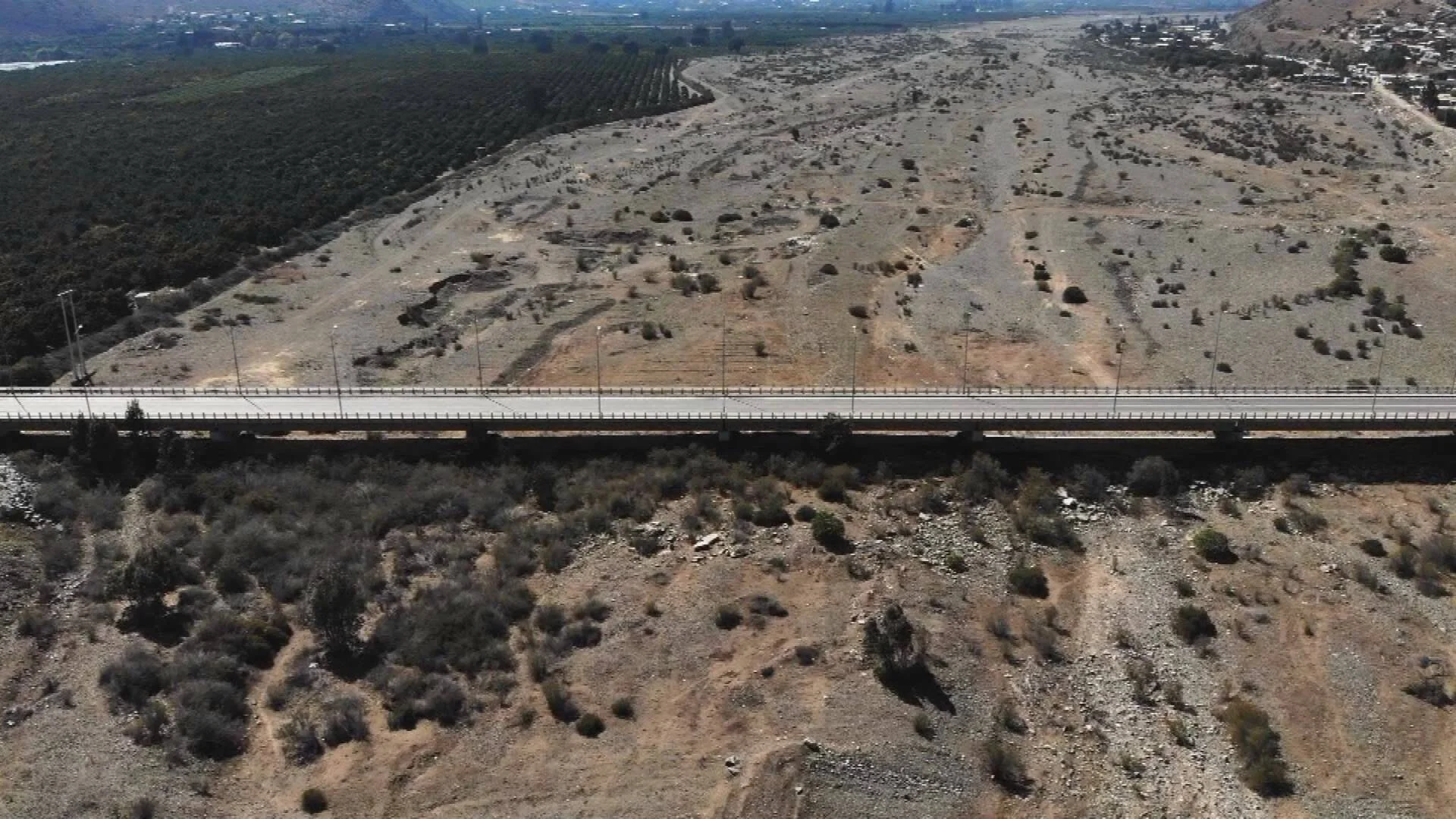 Vista aérea de un puente vial que atraviesa un cauce de río seco rodeado de terreno árido y vegetación escasa.