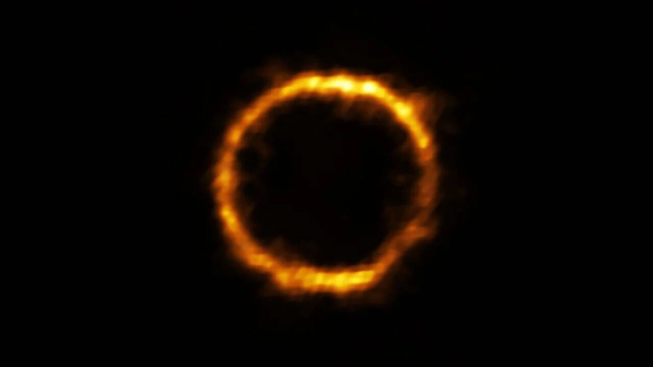 Anillo de Einstein formado por el efecto de lente gravitacional que distorsiona la luz de una galaxia lejana en un anillo luminoso anaranjado sobre fondo negro.