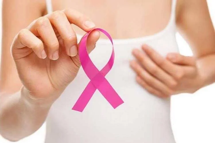Mujer sostiene un lazo rosa, símbolo de concientización sobre el cáncer de mama, frente a su pecho.