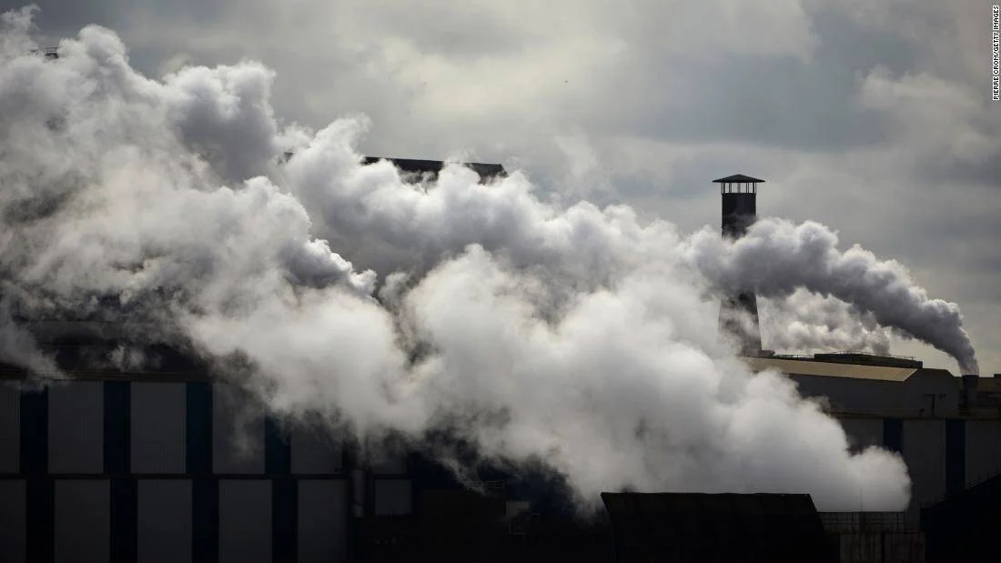 Densas columnas de humo blanco envuelven una planta industrial bajo un cielo nublado, evidenciando contaminación atmosférica.