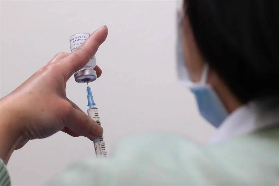 Profesional de salud con mascarilla extrae vacuna de un vial con una jeringa.