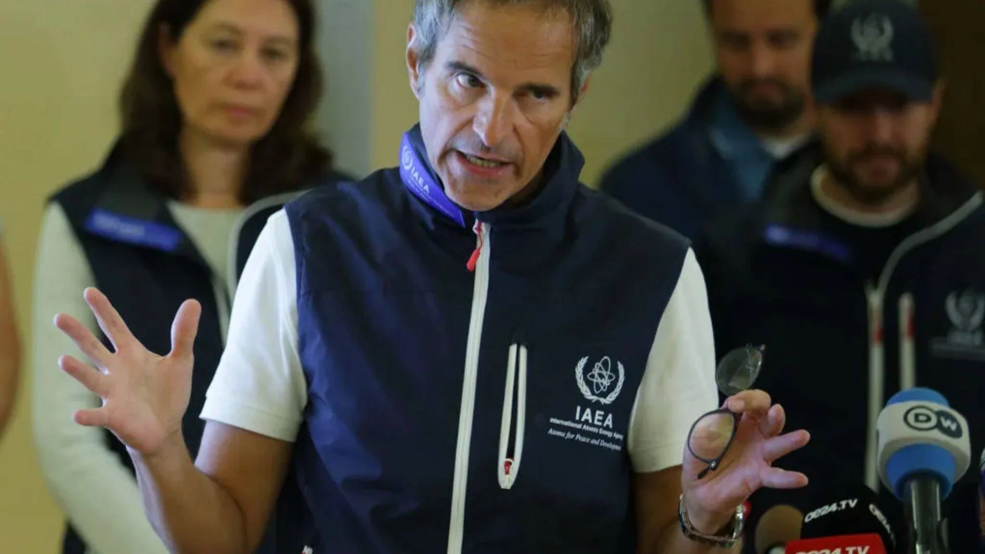 Un hombre con chaleco del OIEA gesticula durante una declaración ante micrófonos de medios internacionales, acompañado por colegas.