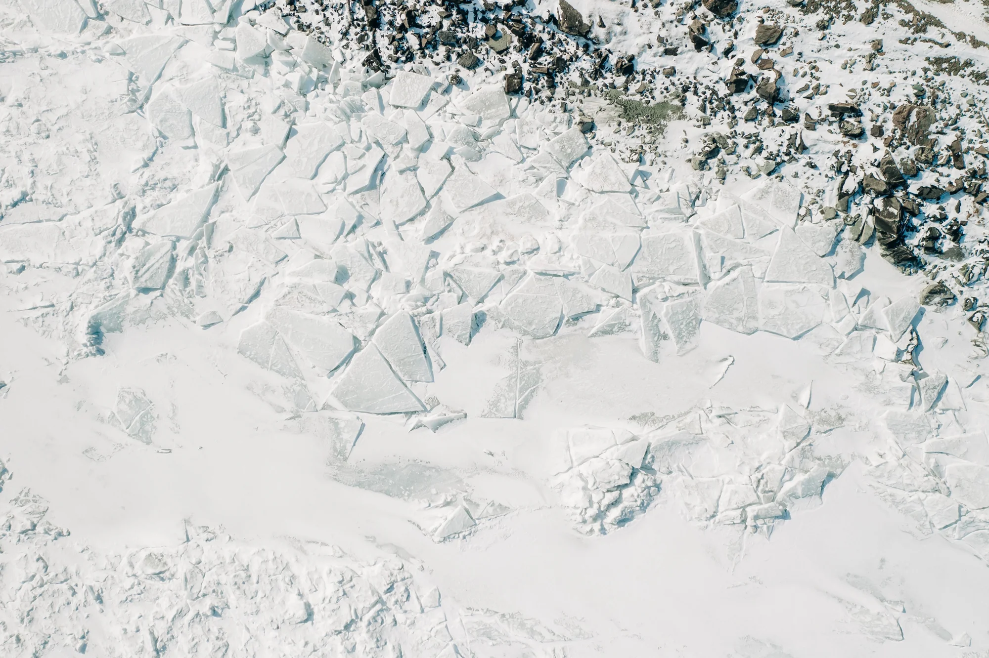 Placas de hielo agrietadas y fragmentadas vistas desde el aire, con rocas nevadas en la orilla.