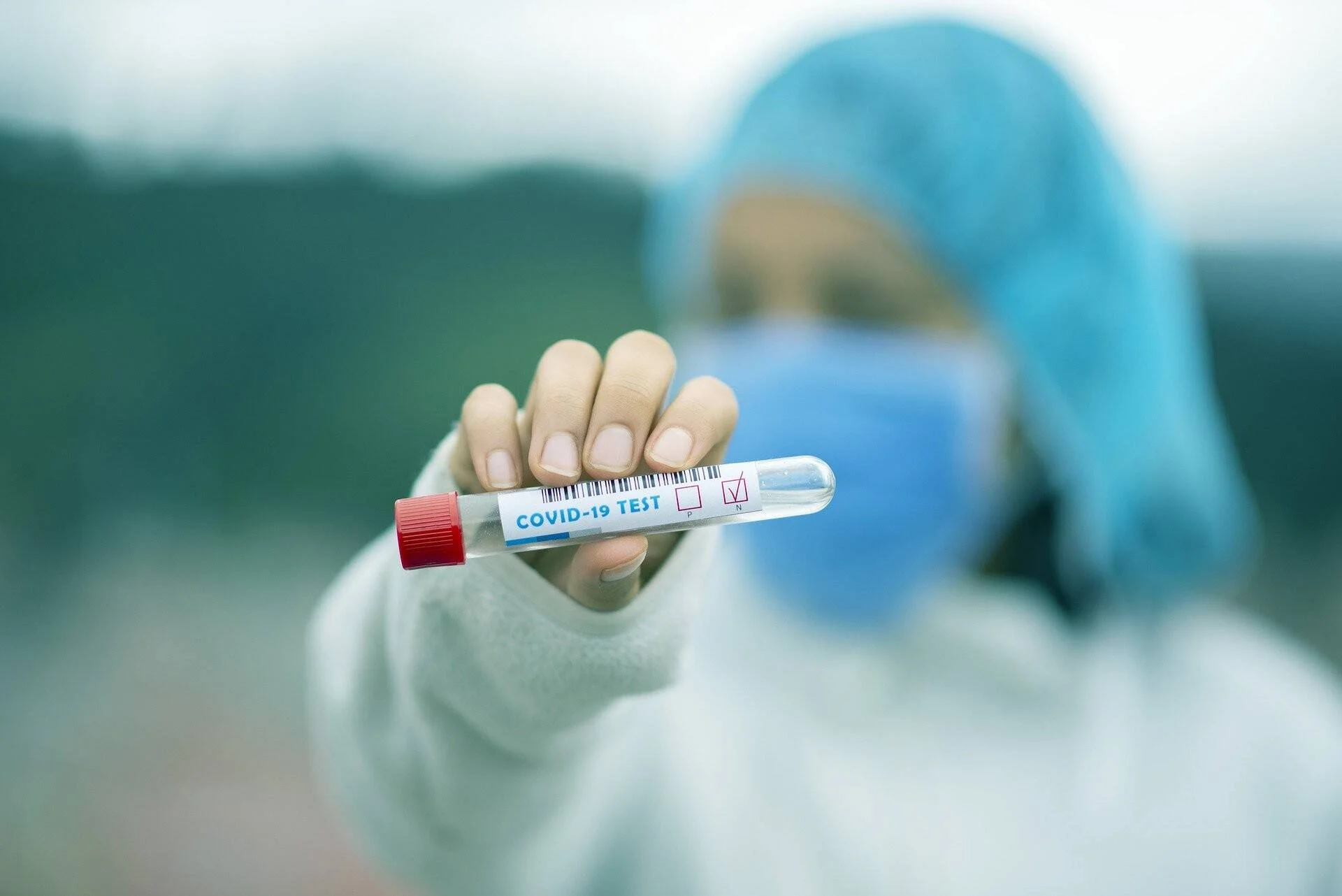 Personal sanitario con equipo de protección muestra un tubo de ensayo etiquetado como prueba COVID-19 con resultado positivo marcado.