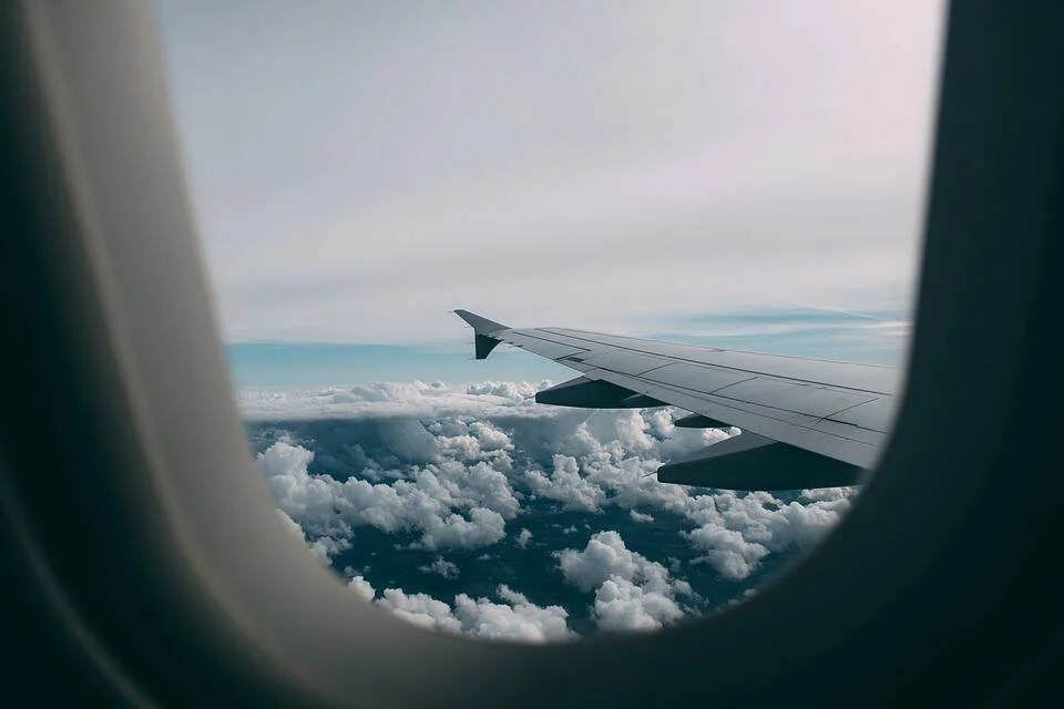 Vista desde la ventanilla de un avión mostrando el ala y un manto de nubes blancas bajo un cielo azul.