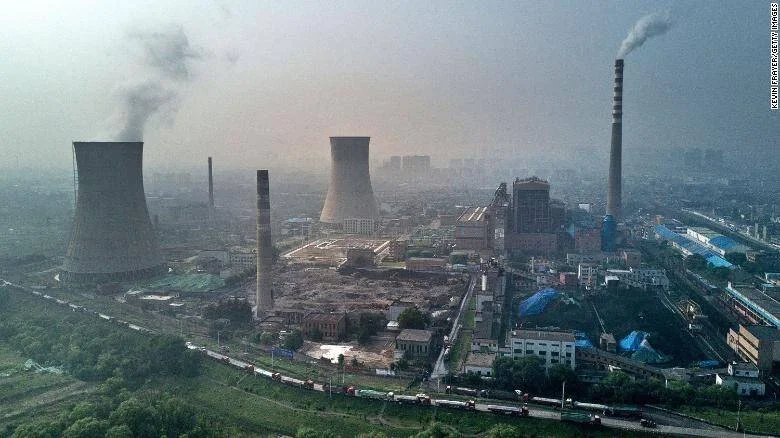 Vista aérea de una central eléctrica de carbón con torres de enfriamiento emitiendo humo en una ciudad industrializada de China.