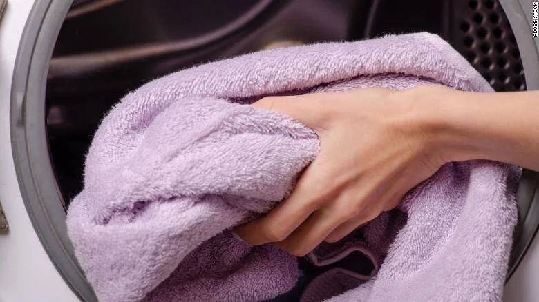 Una mano coloca una toalla de color lila dentro del tambor de una lavadora.