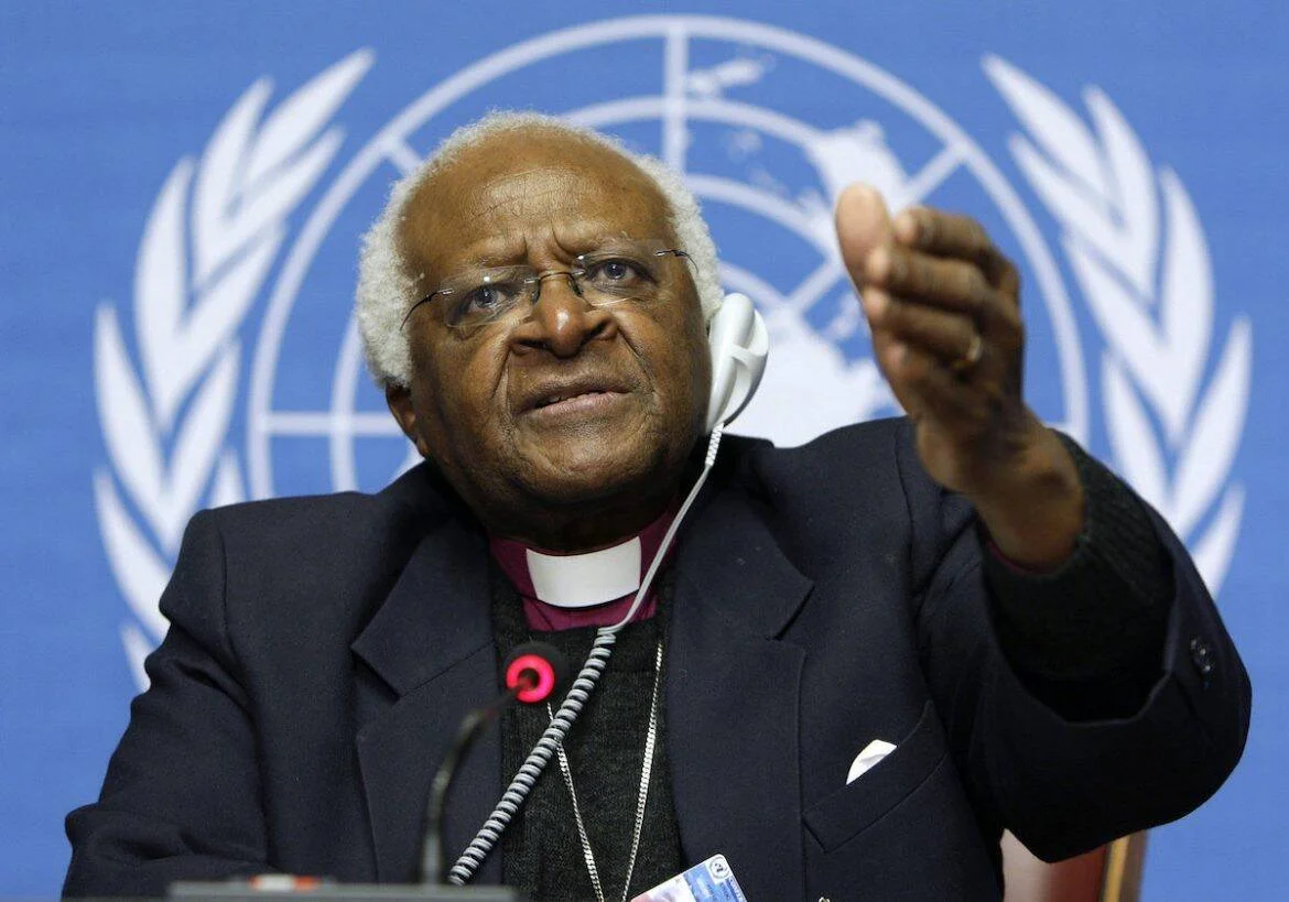 Arzobispo anglicano con vestiduras episcopales gesticula durante una intervención frente al logo de las Naciones Unidas.