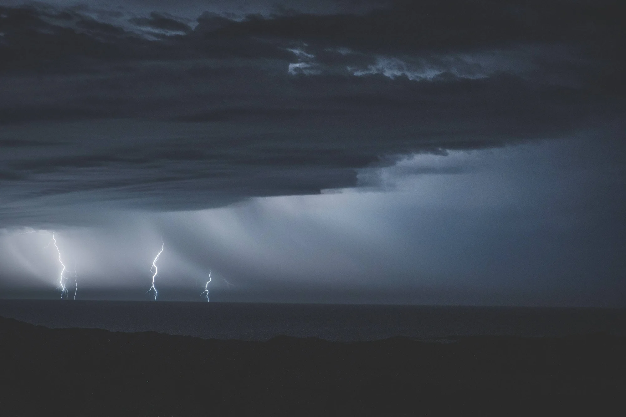 Tres rayos simultáneos iluminan un cielo nocturno con nubes de tormenta sobre un horizonte oscuro.