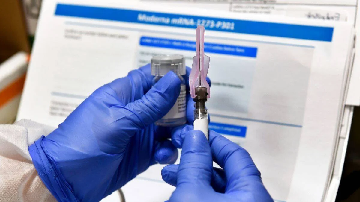 Manos con guantes azules preparan una jeringa frente a un documento del ensayo clínico de la vacuna Moderna mRNA-1273-P301.