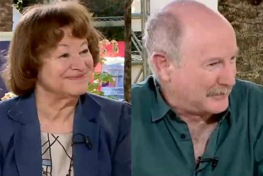 Mujer mayor con saco azul y hombre mayor con bigote, captados en una entrevista televisiva al aire libre.