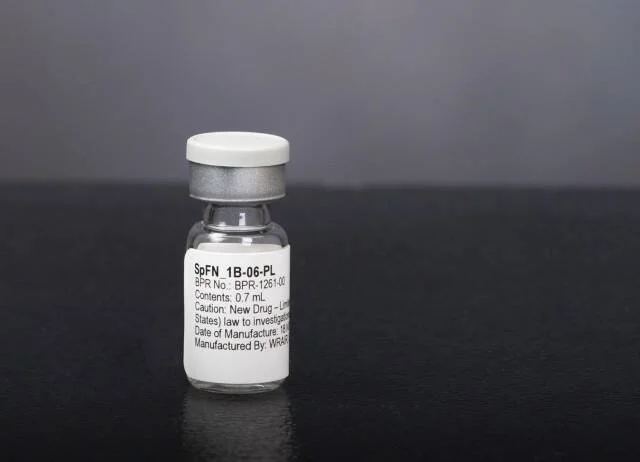 Frasco pequeño de vidrio con tapa blanca etiquetado como SpFN 1B-06-PL, descrito como nuevo fármaco en investigación, sobre superficie oscura.
