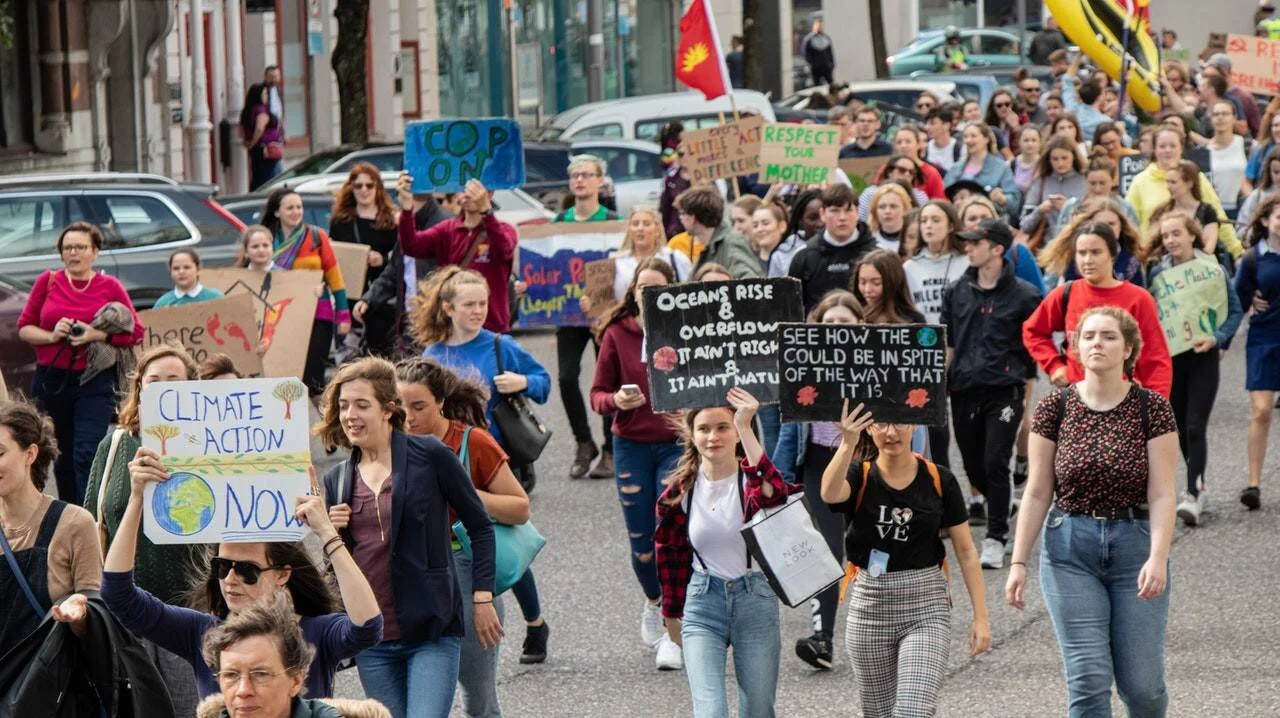 Multitud de jóvenes marcha por una calle con carteles que exigen acción climática inmediata y respeto al medio ambiente.