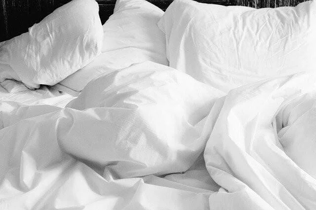 Cama sin tender con sábanas y almohadas blancas arrugadas tras ser usada.